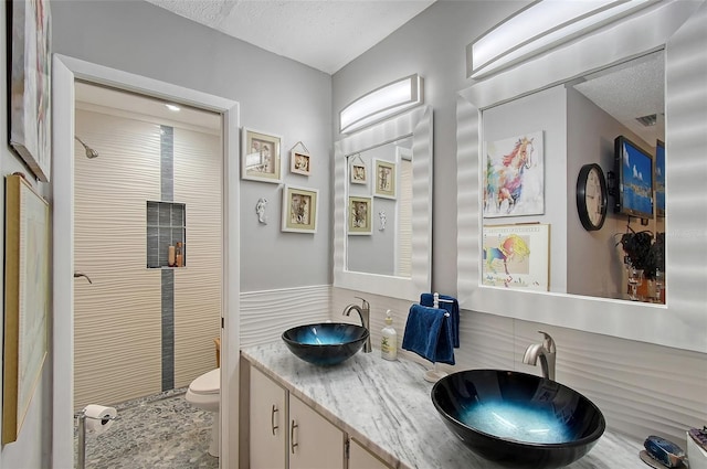 bathroom featuring a tile shower, vanity, a textured ceiling, and toilet