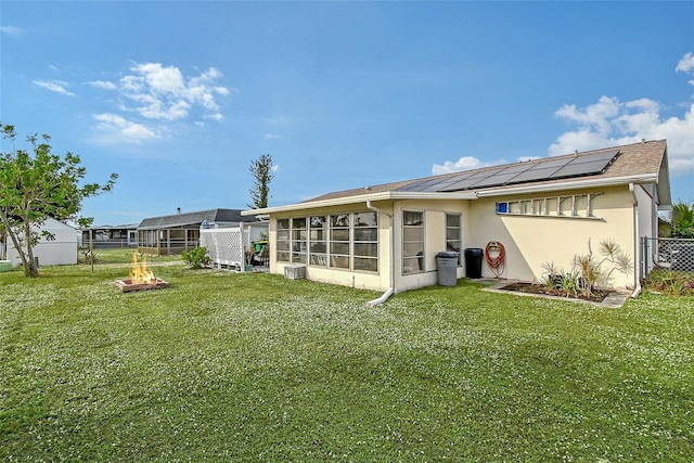 rear view of house with a sunroom, solar panels, an outdoor fire pit, and a lawn