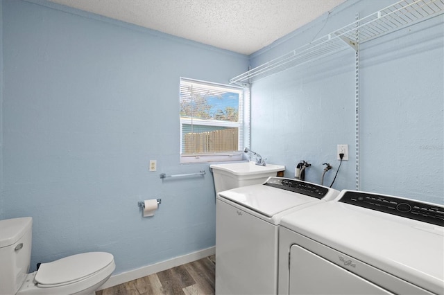 clothes washing area featuring wood-type flooring, a textured ceiling, washer and clothes dryer, and sink