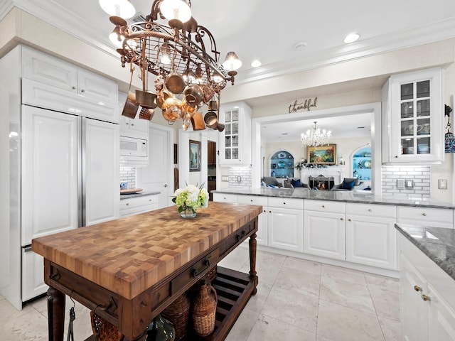 kitchen with built in appliances, light stone counters, tasteful backsplash, and white cabinetry