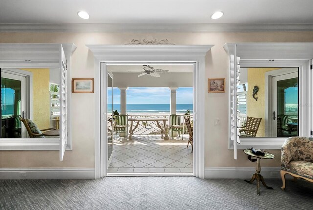 doorway to outside with a view of the beach, carpet, a water view, crown molding, and ceiling fan