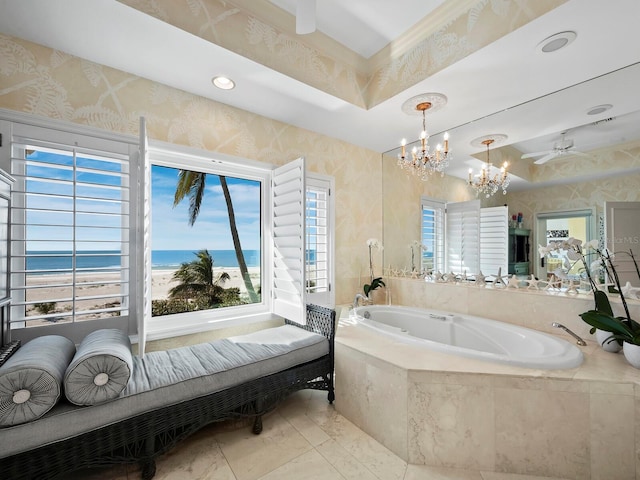 bathroom with a raised ceiling, tiled tub, a notable chandelier, and a water view