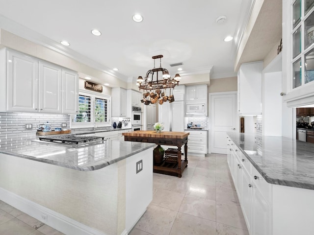 kitchen featuring appliances with stainless steel finishes, a peninsula, crown molding, and white cabinetry