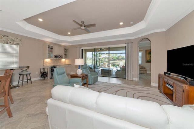 living room with a tray ceiling, beverage cooler, ornamental molding, and ceiling fan