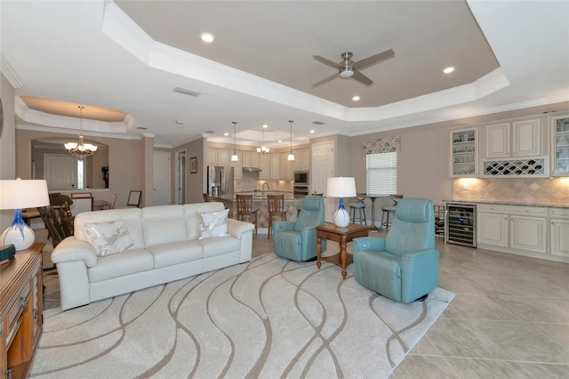 living room featuring ceiling fan with notable chandelier, wine cooler, a raised ceiling, and crown molding