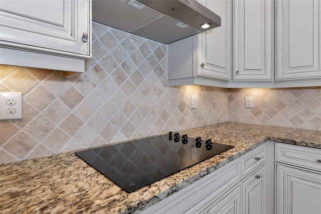 kitchen with backsplash, wall chimney exhaust hood, black electric cooktop, light stone counters, and white cabinetry