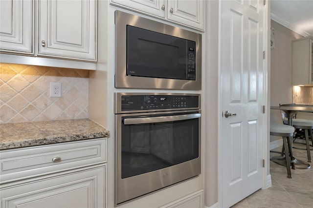 kitchen with backsplash, light stone counters, built in microwave, crown molding, and white cabinets