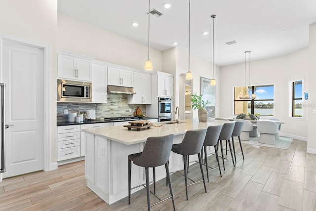 kitchen featuring hanging light fixtures, stainless steel appliances, an island with sink, a breakfast bar, and white cabinets