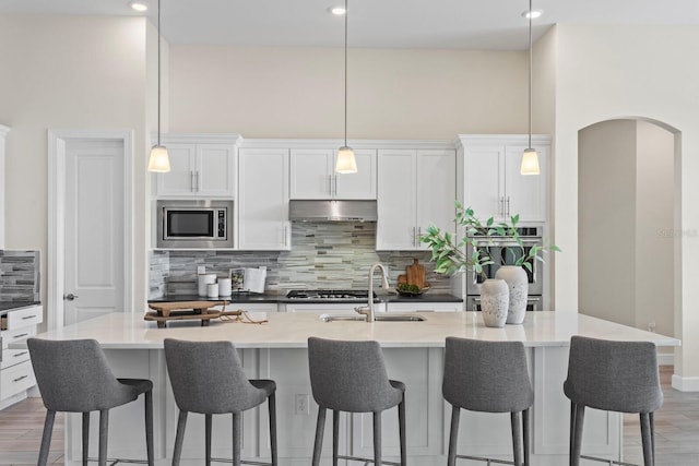 kitchen featuring stainless steel microwave, decorative backsplash, a center island with sink, and decorative light fixtures