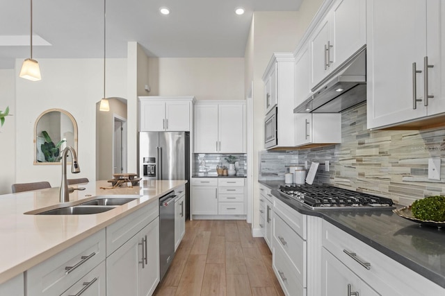 kitchen with backsplash, sink, appliances with stainless steel finishes, decorative light fixtures, and white cabinetry