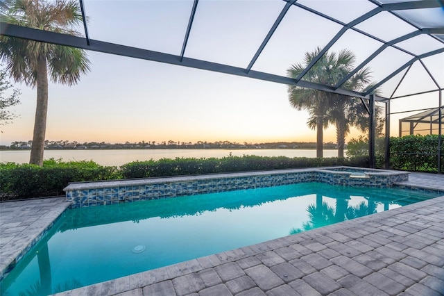 pool at dusk featuring a lanai, an in ground hot tub, a water view, and a patio