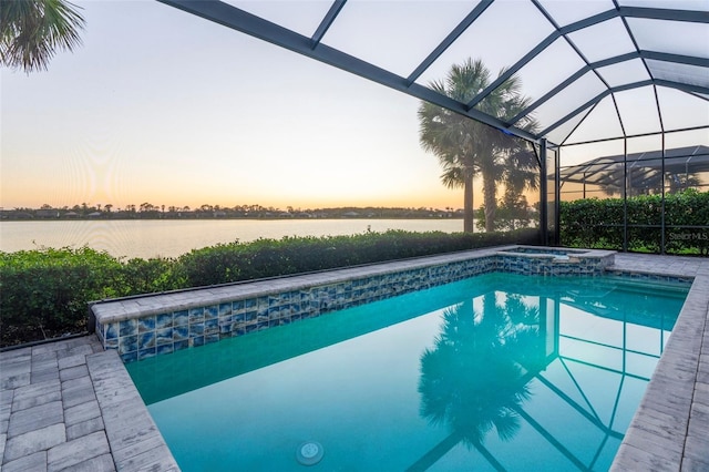 pool at dusk featuring glass enclosure, a water view, and an in ground hot tub