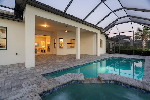 pool at dusk with glass enclosure and a patio area