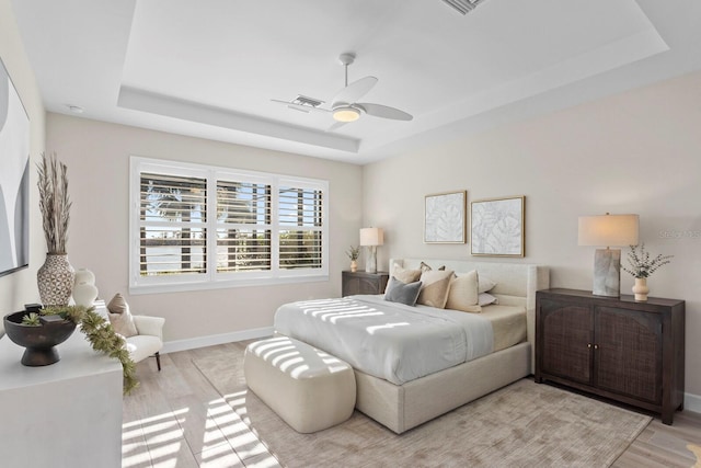 bedroom with a raised ceiling, ceiling fan, and light hardwood / wood-style flooring