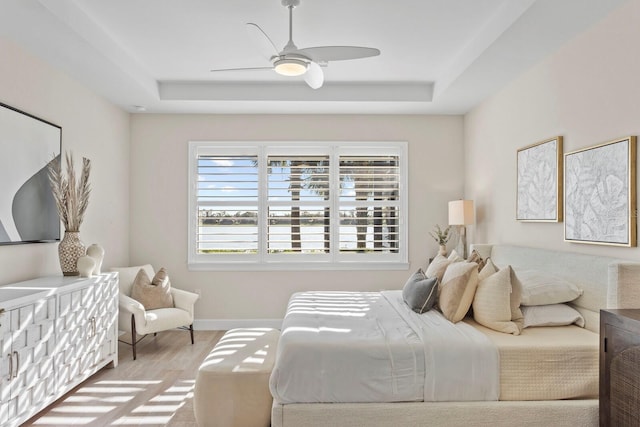 bedroom featuring a tray ceiling, ceiling fan, and light hardwood / wood-style flooring