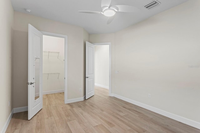 unfurnished bedroom with light wood-type flooring, a walk in closet, a closet, and ceiling fan