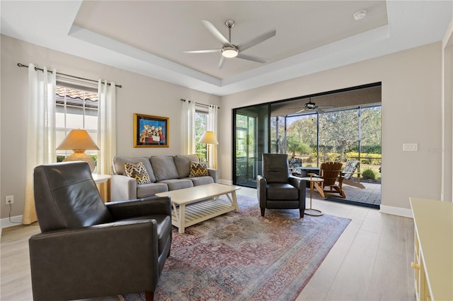 living room featuring ceiling fan, light hardwood / wood-style floors, and a raised ceiling