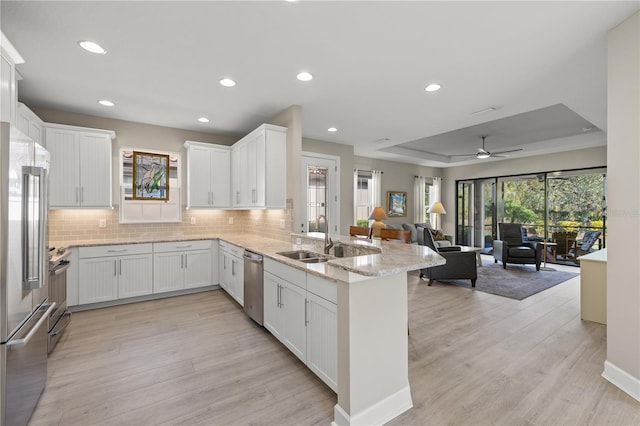 kitchen with kitchen peninsula, a tray ceiling, ceiling fan, sink, and white cabinets