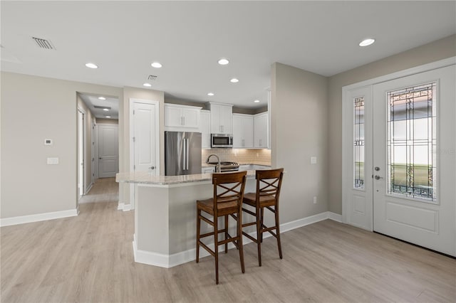 kitchen featuring appliances with stainless steel finishes, light stone counters, light hardwood / wood-style floors, white cabinetry, and a breakfast bar area