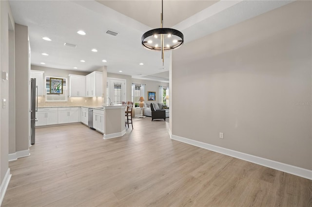 kitchen featuring kitchen peninsula, light wood-type flooring, stainless steel appliances, white cabinetry, and hanging light fixtures