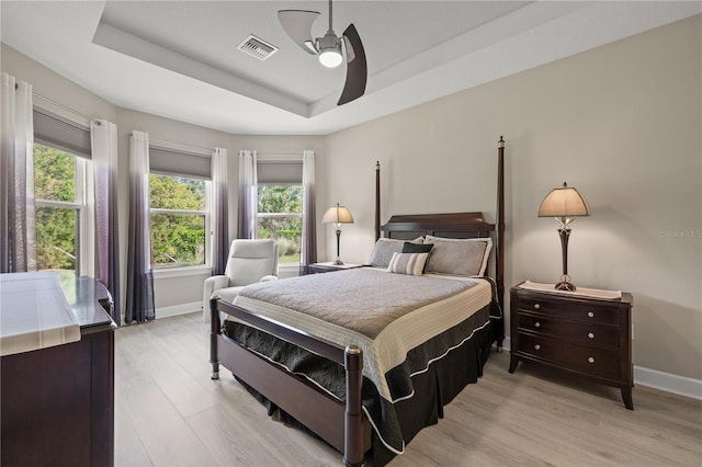 bedroom with ceiling fan, a raised ceiling, and light wood-type flooring