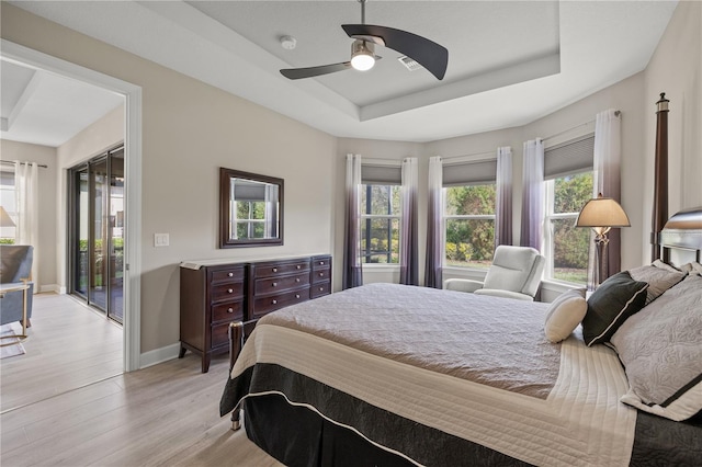 bedroom featuring access to exterior, light hardwood / wood-style floors, a raised ceiling, and ceiling fan