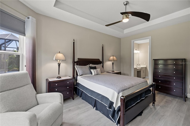 bedroom featuring ceiling fan, light hardwood / wood-style floors, a raised ceiling, and connected bathroom