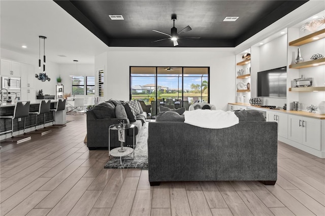 living room featuring ceiling fan and a raised ceiling