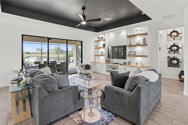 living room with a raised ceiling, ceiling fan, and light wood-type flooring