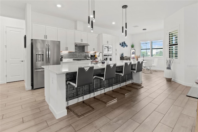 kitchen featuring a kitchen breakfast bar, stainless steel appliances, pendant lighting, a large island with sink, and white cabinetry