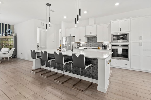 kitchen featuring a large island with sink, decorative light fixtures, a breakfast bar area, white cabinets, and appliances with stainless steel finishes