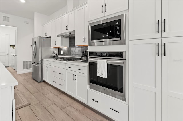 kitchen with decorative backsplash, white cabinets, and appliances with stainless steel finishes