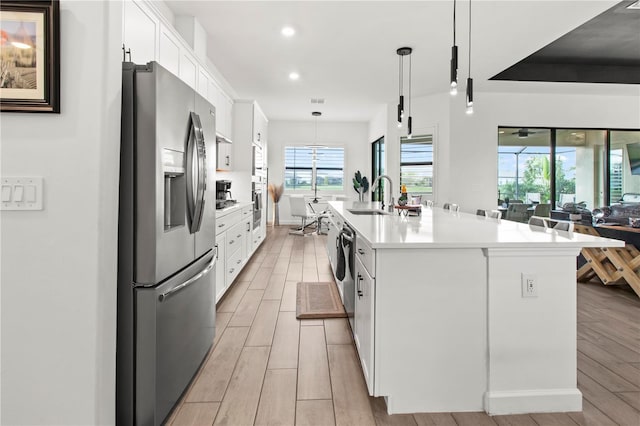 kitchen featuring white cabinetry, hanging light fixtures, stainless steel appliances, and a center island with sink