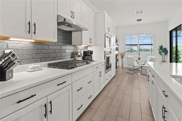 kitchen featuring tasteful backsplash, pendant lighting, white cabinets, and stainless steel appliances