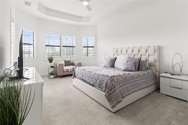 carpeted bedroom with multiple windows, a raised ceiling, and ceiling fan