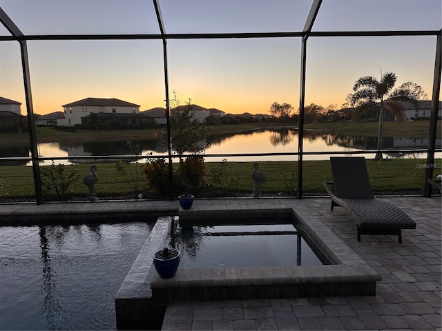 pool at dusk with a water view, a patio area, and a lanai