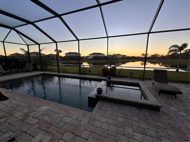 pool at dusk featuring a lanai, a patio area, and a water view