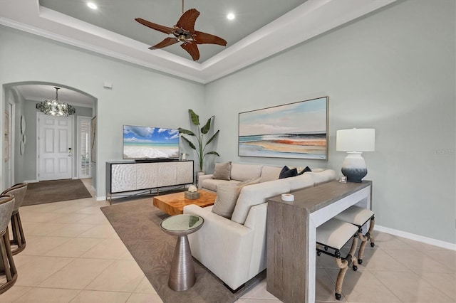 living room featuring ceiling fan with notable chandelier, light tile patterned floors, ornamental molding, and a tray ceiling