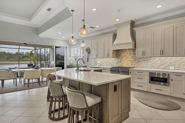 kitchen featuring decorative light fixtures, a center island with sink, light tile patterned floors, custom range hood, and sink