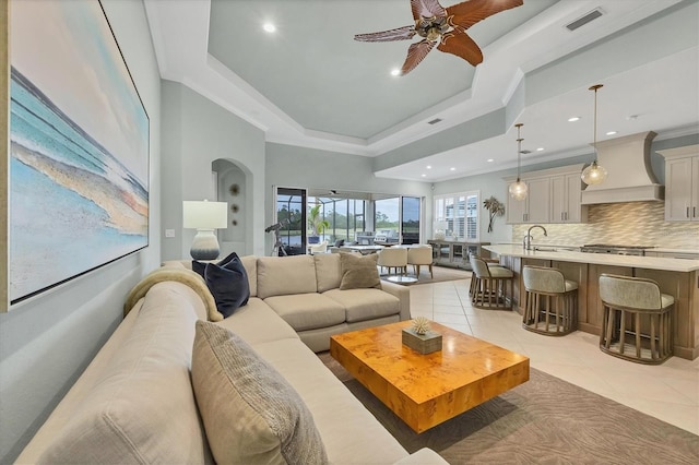 tiled living room with ceiling fan, a tray ceiling, and sink