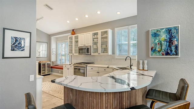 kitchen with lofted ceiling, kitchen peninsula, a kitchen bar, sink, and appliances with stainless steel finishes