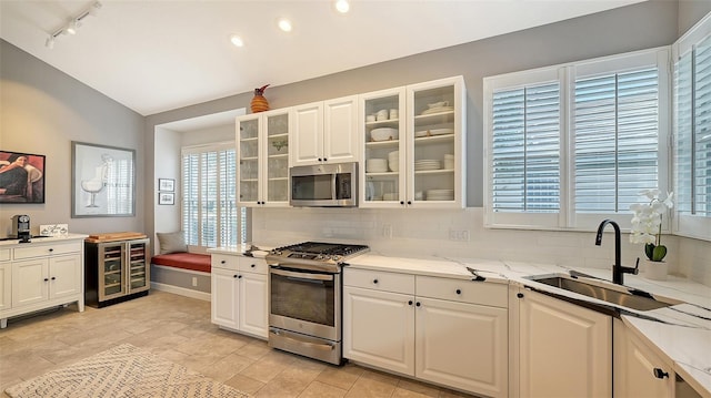 kitchen with vaulted ceiling, sink, appliances with stainless steel finishes, white cabinets, and beverage cooler