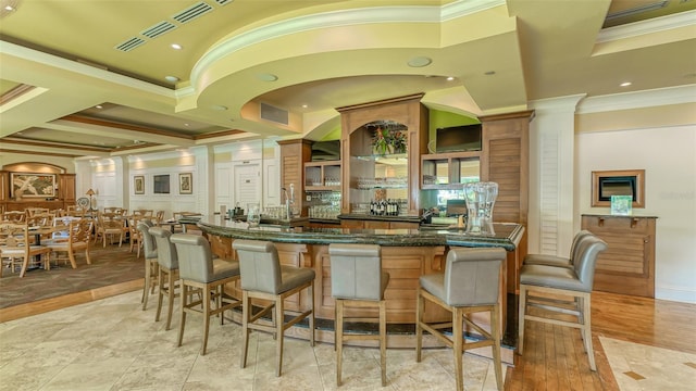 bar with light tile patterned floors, dark stone counters, crown molding, and ornate columns