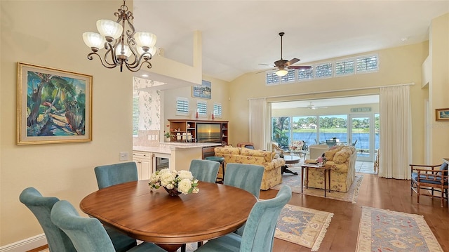 dining space featuring lofted ceiling, hardwood / wood-style floors, beverage cooler, and ceiling fan with notable chandelier