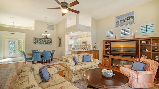 living room featuring a towering ceiling, ceiling fan with notable chandelier, and light wood-type flooring