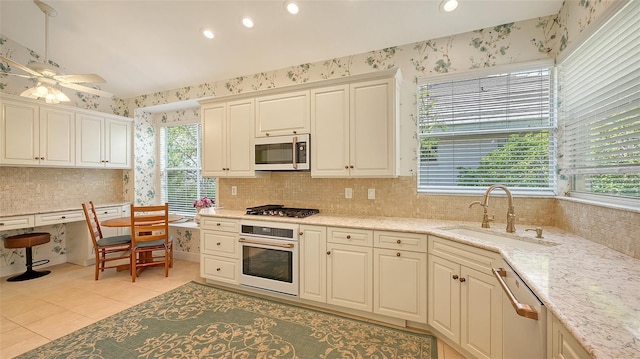 kitchen with sink, ceiling fan, light tile patterned flooring, light stone counters, and stainless steel appliances