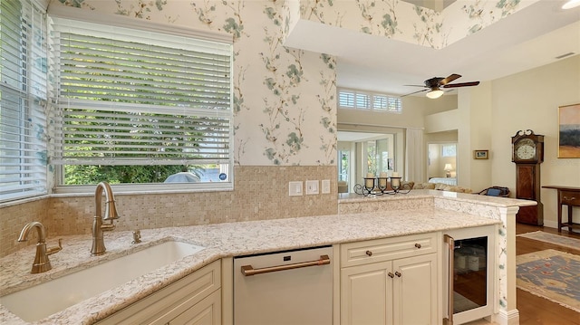 kitchen with sink, beverage cooler, light stone counters, stainless steel dishwasher, and backsplash