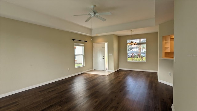 empty room with ceiling fan with notable chandelier, a wealth of natural light, and dark wood-type flooring