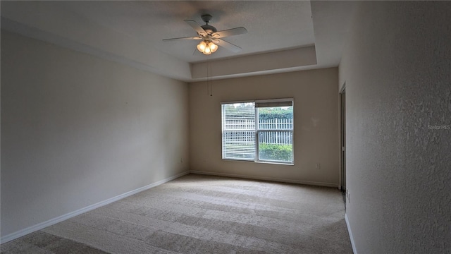 carpeted spare room with a raised ceiling and ceiling fan