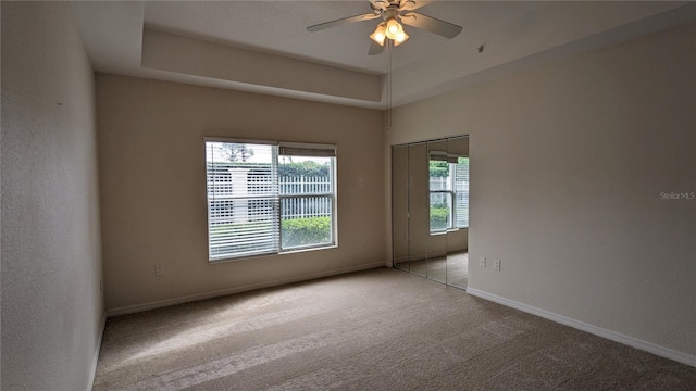 empty room featuring ceiling fan, a raised ceiling, and light carpet